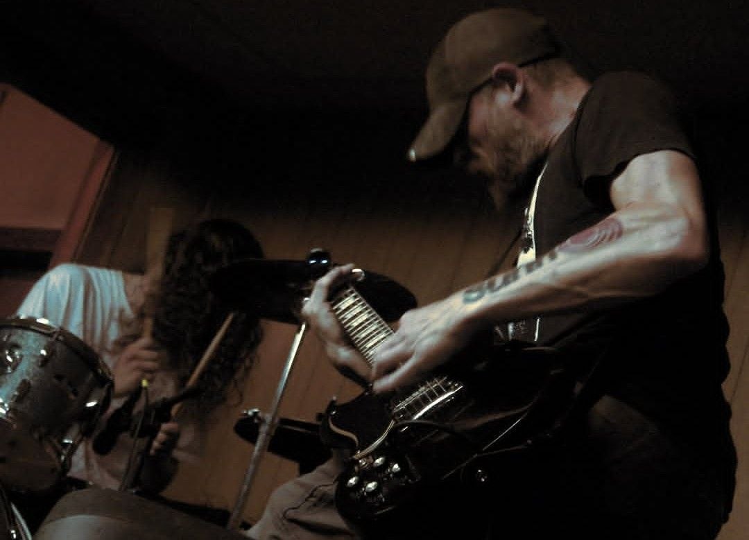 Dark warm-lit shot of guitarist and drummer playing together